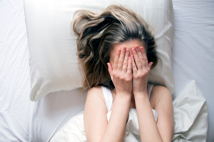 Woman in bed, sad, with hands over face
