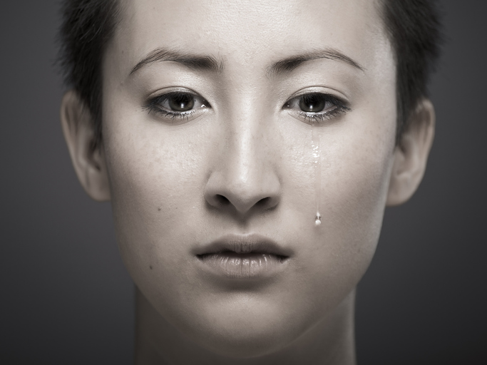 A desaturated photo of a young woman with short hair. A single tear rolls down her cheek.