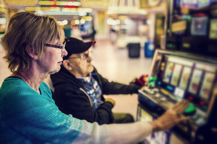 An older woman plays a slot machine while looking bored.