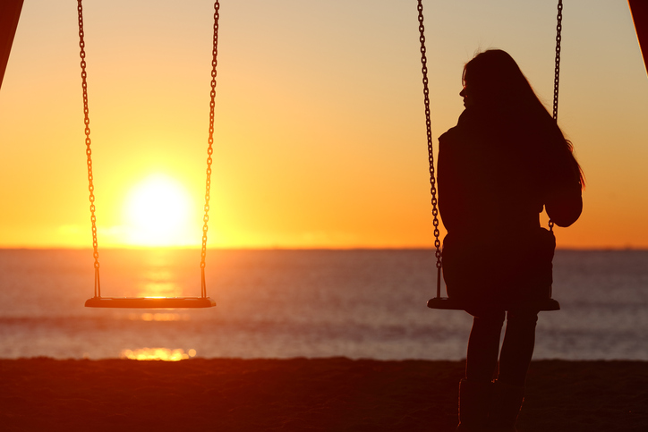 A young woman swings alone, looking at the empty swing beside her.