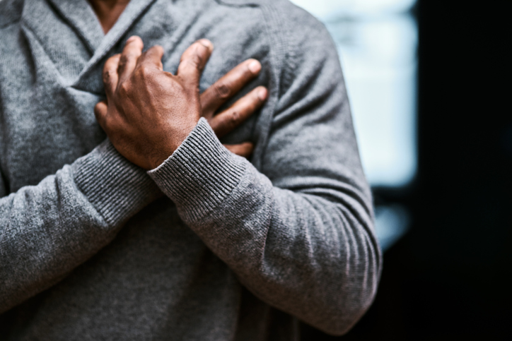 A man in a gray sweater grips his chest in pain.