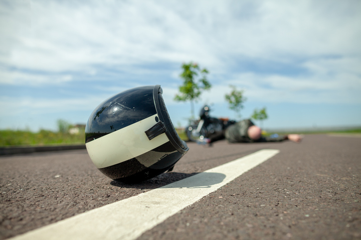 Close-up of helmet on the road, with a motorcycle and its rider lying prone in the background.