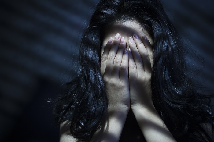 Woman hiding her face with her hands in a dark room