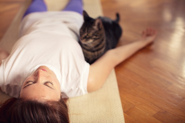 Woman lying on yoga mat next to cat