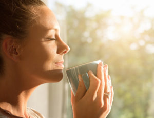 Woman takes a moment to enjoy her coffee and the sunlight on her face.