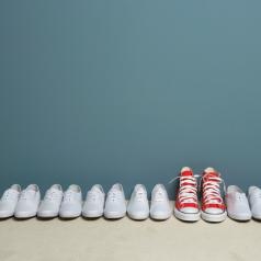One pair of red shoes stands out in row of white shoes along wall