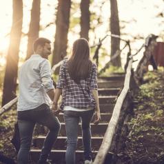 Rear view of couple talking as they hold hands and climb stairs along forest trail