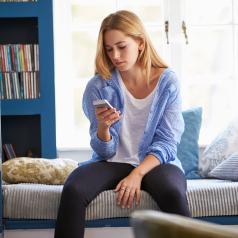 Woman sitting on bed while looking at phone